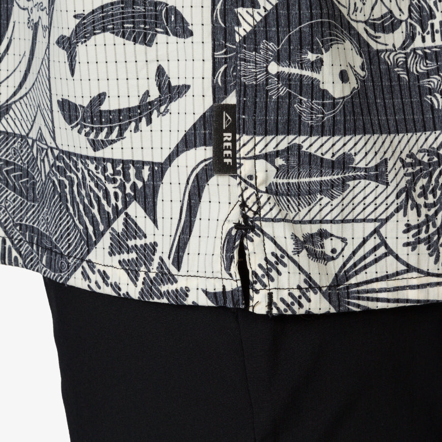 Close-up of the lower hem of the Beckham Camp Shirt showing ocean-inspired print and REEF brand tag on men's apparel.