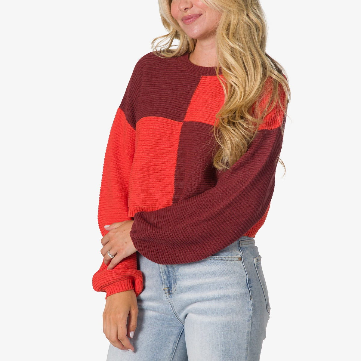 Woman wearing a red and burgundy checkered Carrie Sweater with long sleeves, shown from the front waist up in a casual pose.