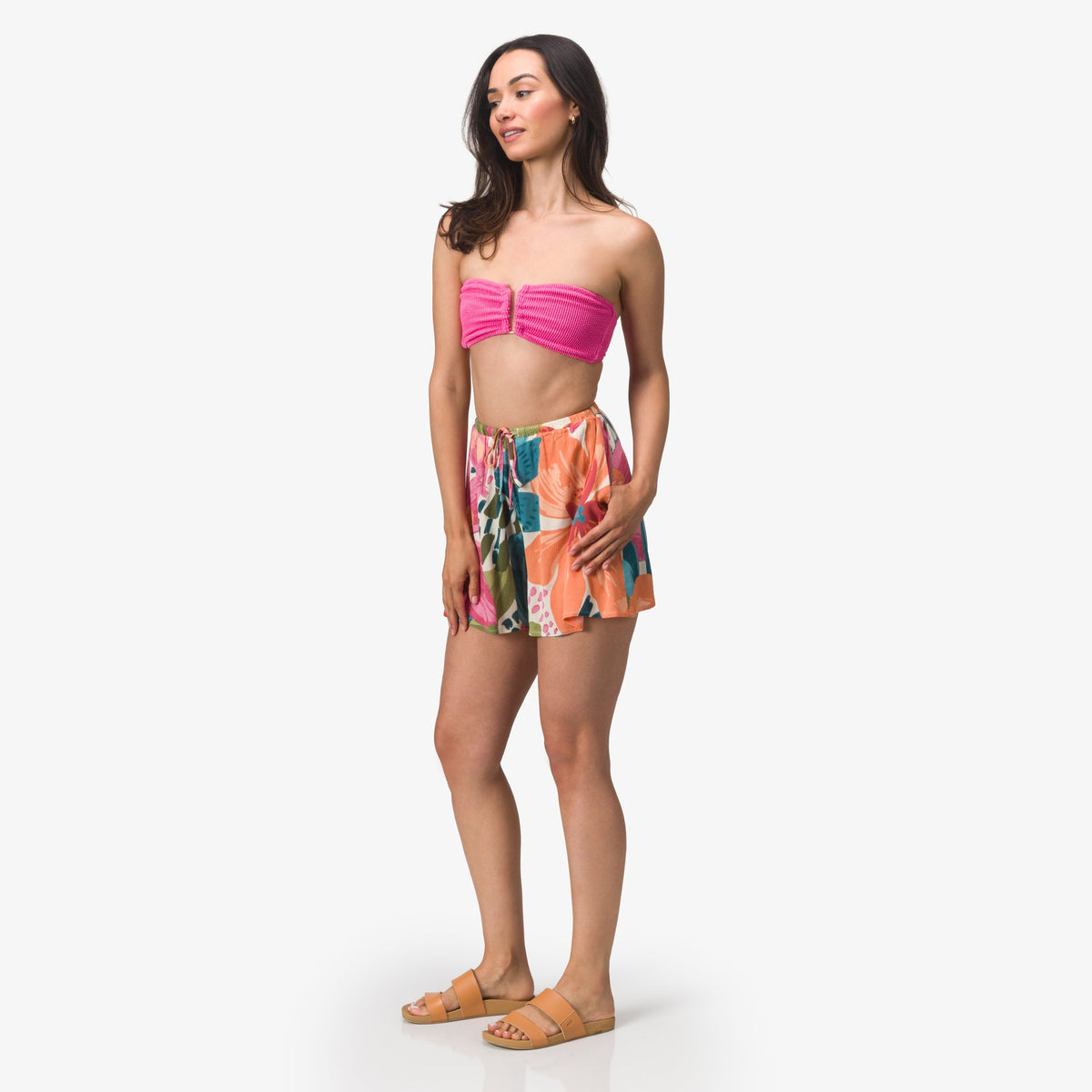 Woman wearing Eve Flutter Short with vibrant floral pattern standing facing left in casual beach apparel and sandals