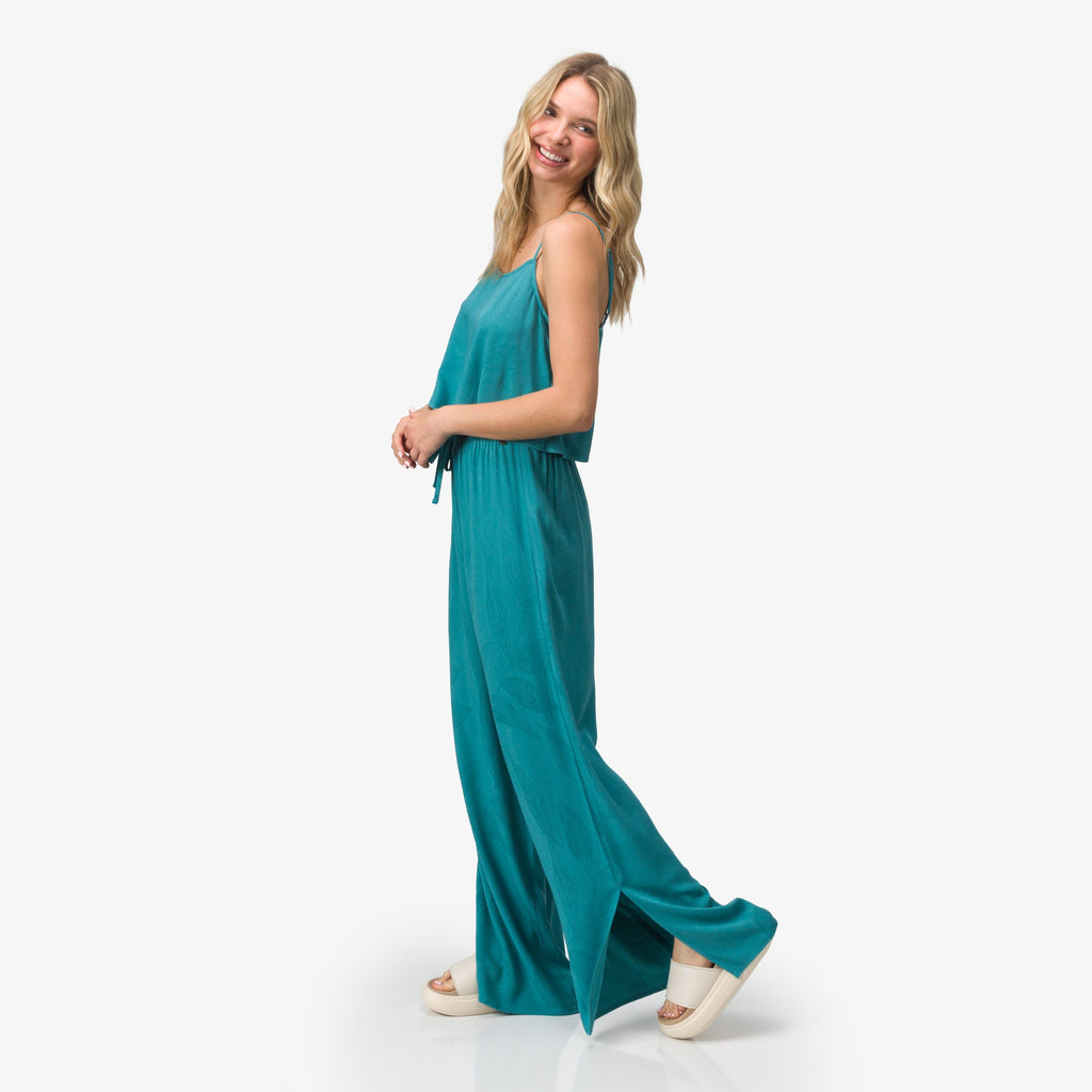 Woman wearing teal Ollie Pant in side view with sandals, showcasing relaxed fit and beach-inspired comfortable style.