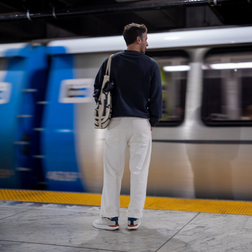 Man wearing Shoreline Del Mar sneakers facing back at platform edge with blue, white, and tan colors, urban travel style.