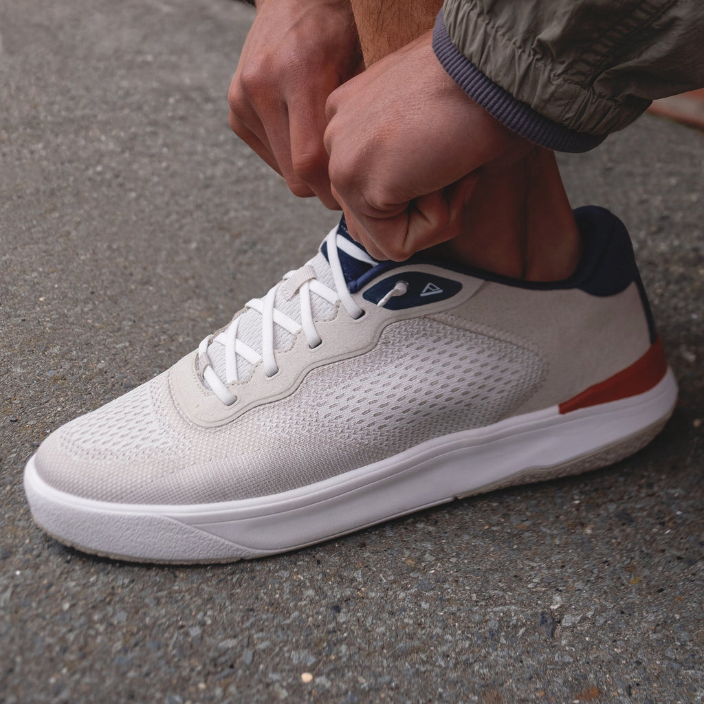 Shoreline Del Mar sneaker facing right, breathable tan knit upper with navy collar, white sole, tying elastic laces.