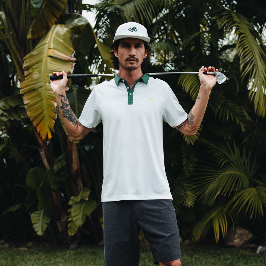Man wearing Blackball Hat facing forward outdoors with tropical plants, surf-inspired comfort and style for active beach lifestyle