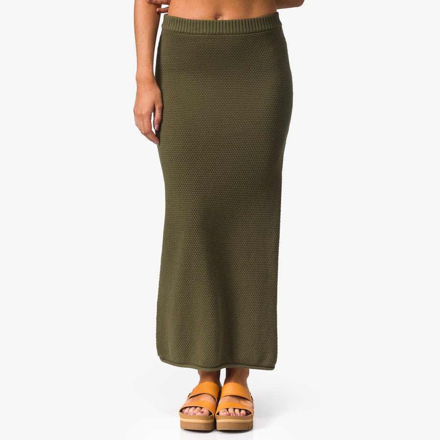Front view of woman wearing olive Up North Sweater Skirt with tan platform sandals facing forward, beach-inspired comfort apparel.