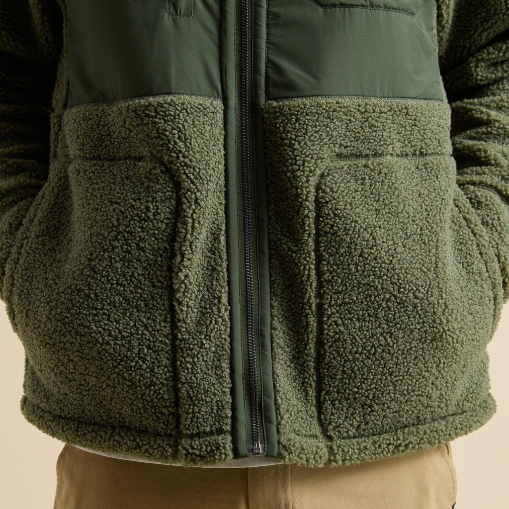 Close-up of front pocket and zipper detail on olive green Cooke Sherpa Jacket, showing soft, textured fleece fabric.