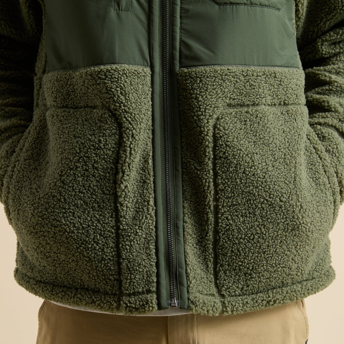 Close-up of front pocket and zipper detail on olive green Cooke Sherpa Jacket, showing soft, textured fleece fabric.