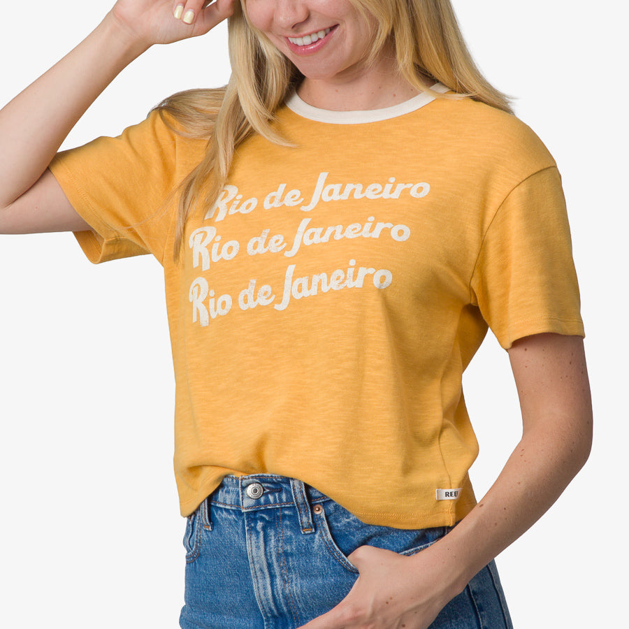 Woman wearing a honey gold Ringer Tee with white collar and Rio de Janeiro print, showing front and upper torso.