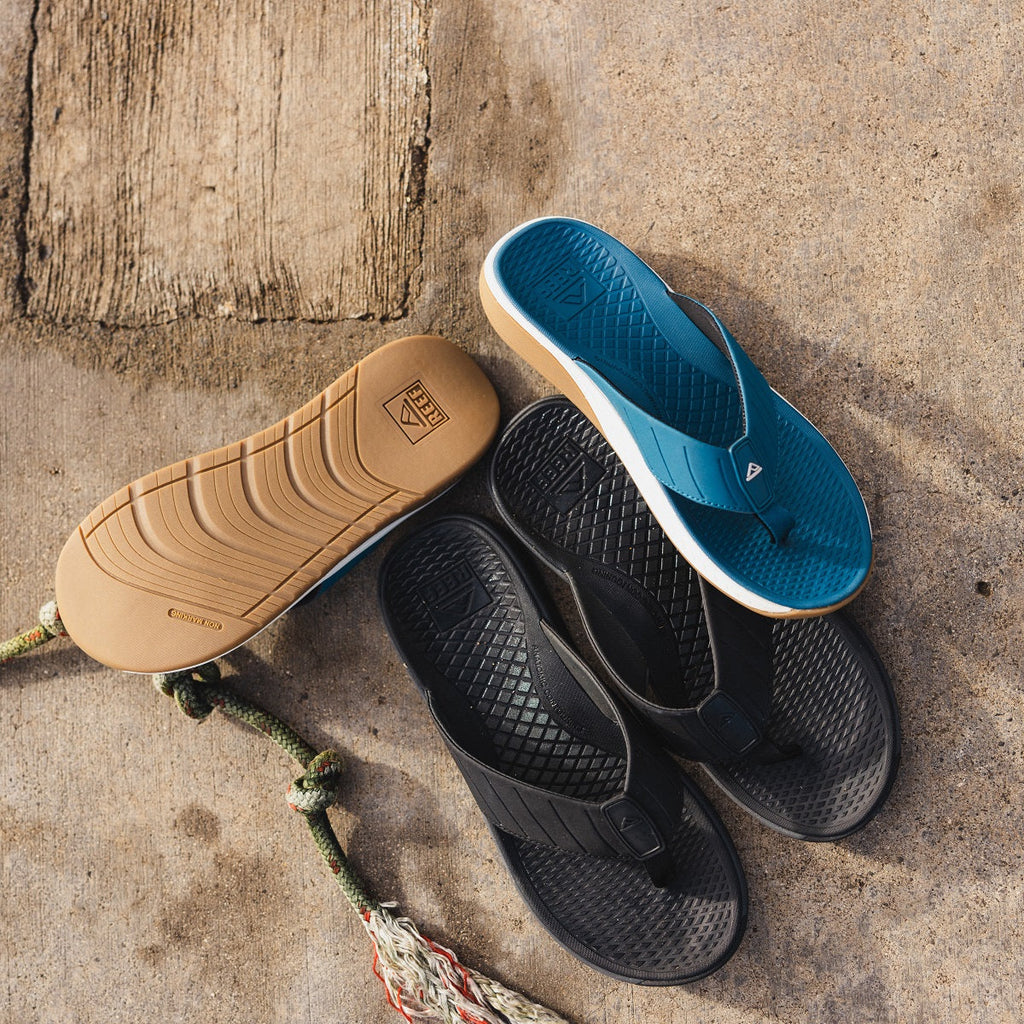 The Deckhand men's blue right-facing flip flop top view with black left-facing flip flop soles showing textured footbeds and rubber outsoles.