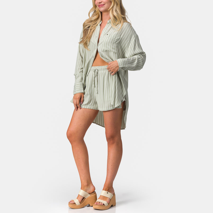 Woman wearing Sandy Stripe Short in desert sage stripe, paired with lightweight shirt, standing in neutral pose facing forward.