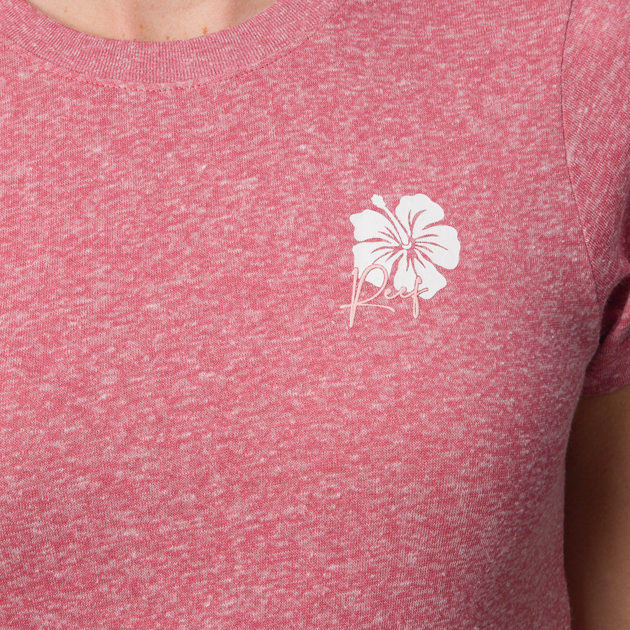 Close-up of a woman's upper torso wearing the mauve Saylor Fitted Tee with a white hibiscus logo, beach-inspired comfort apparel.