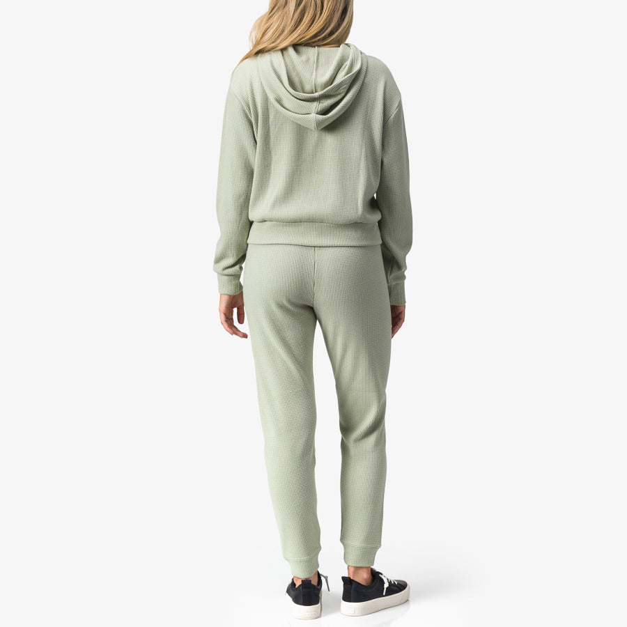 Woman wearing Tina Thermal Hoodie in desert sage, rear view, showcasing comfort-focused, surf-inspired casual apparel.