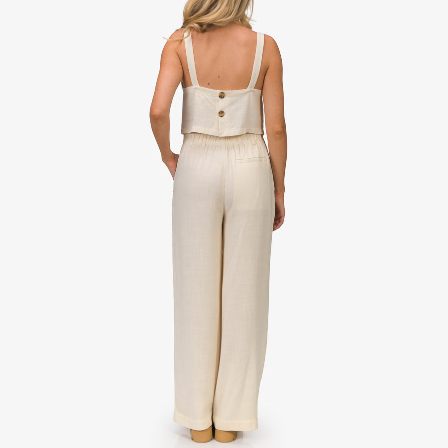 Woman wearing Tori Linen Tank in almond milk, back view, showcasing soft linen fabric and relaxed fit for beach comfort.