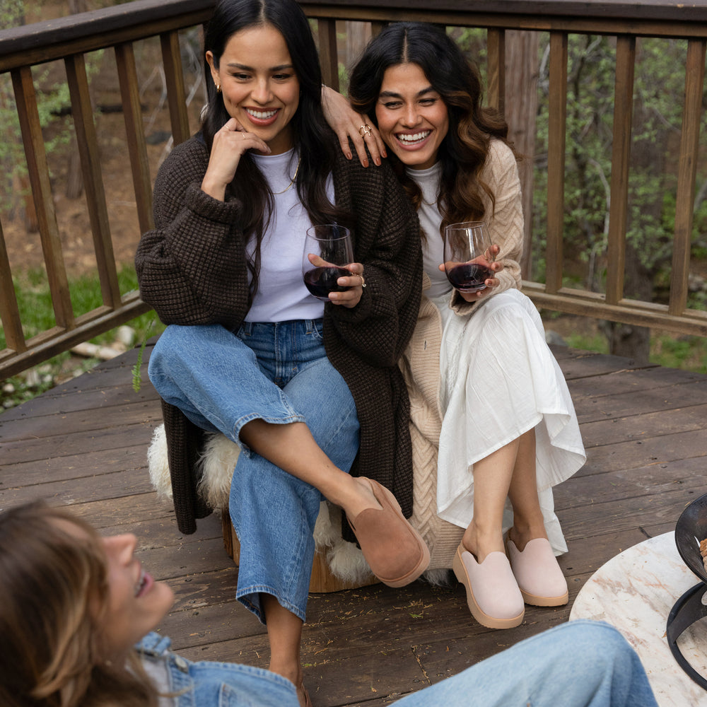 Two women wearing Vista Skye slip-on shoes seated on a deck, right shoe facing forward, left shoe angled slightly outward.