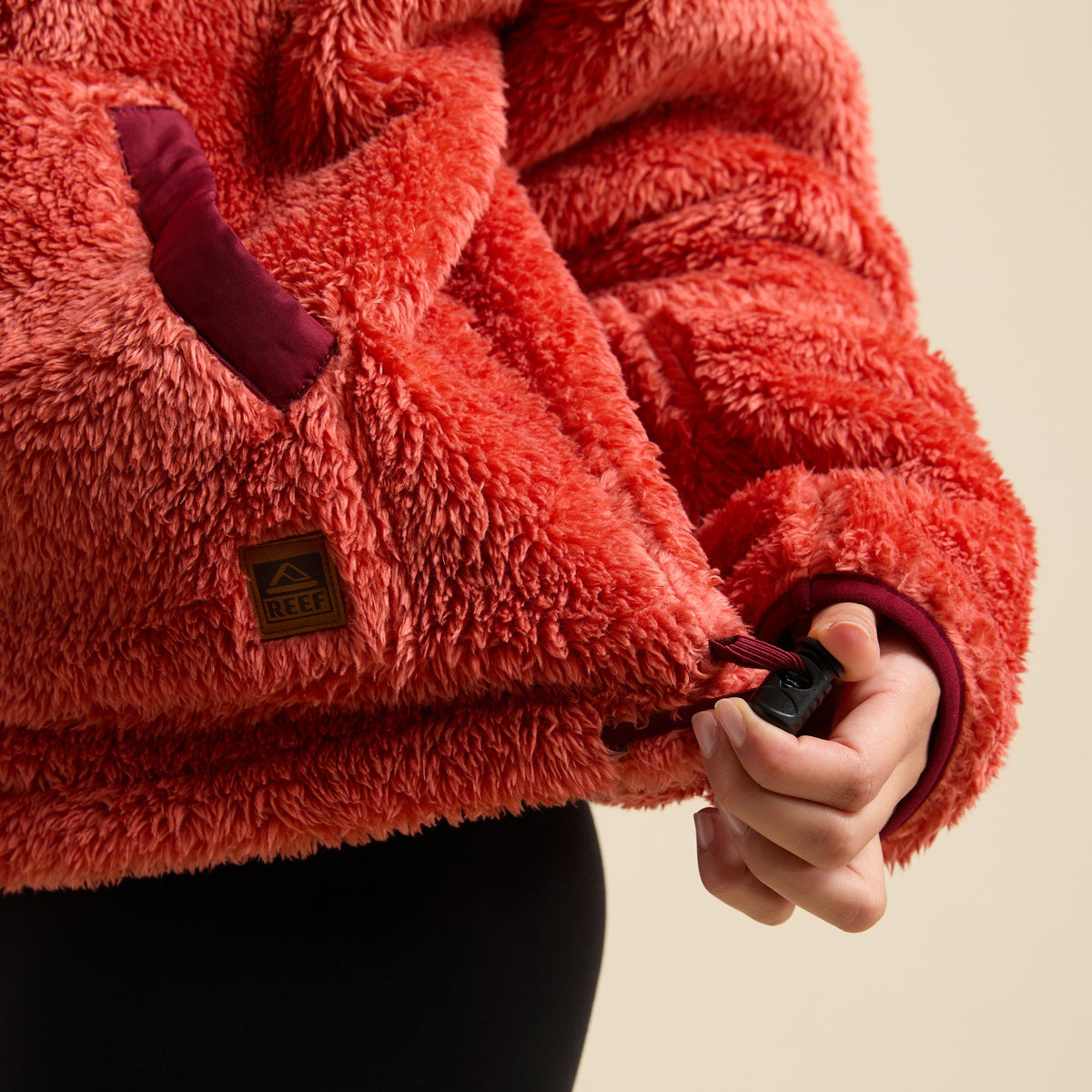 Close-up of a hand adjusting the hem drawstring on a red Pilot Sherpa Jacket pocket with soft fleece texture.