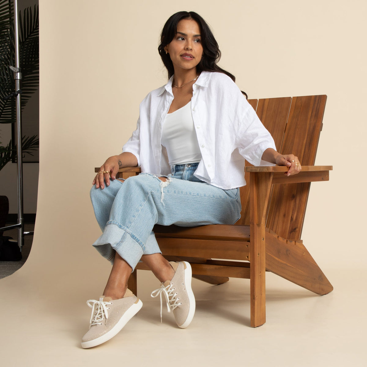 Woman seated on wooden chair wearing Reef Neptune beige sneakers facing left, showcasing comfort and surf-inspired style.